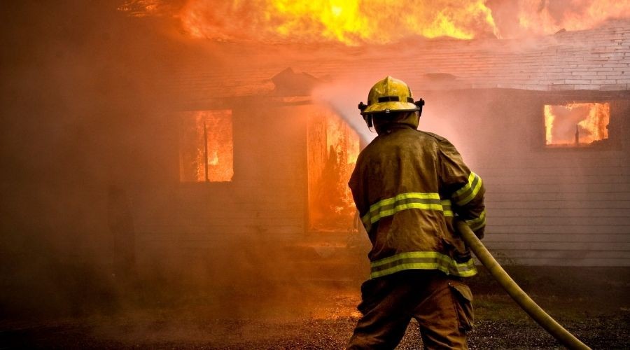 Firefighter battling flames from a burning house, illustrating emergency response and safety.