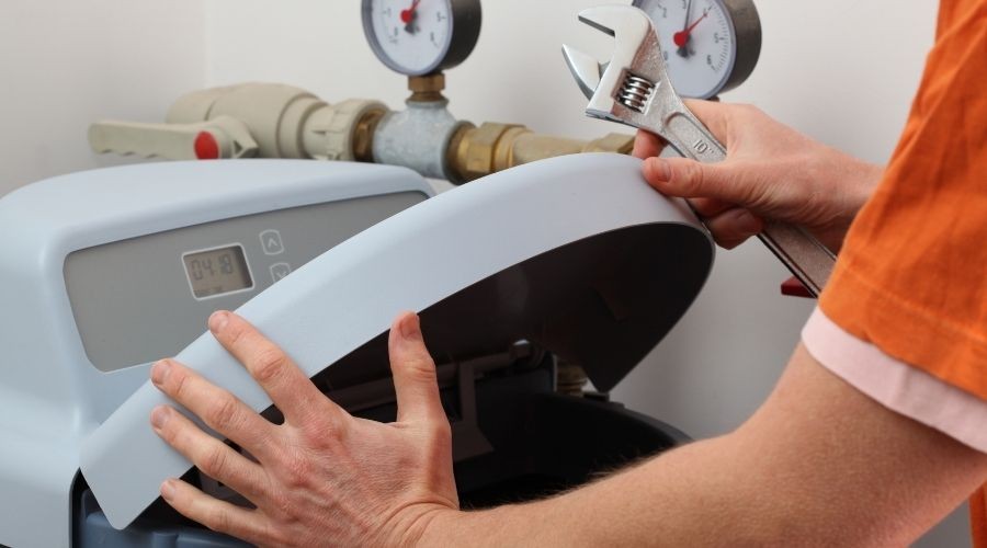 Person using a wrench to open a water softener unit, with pressure gauges visible, illustrating plumbing service maintenance.