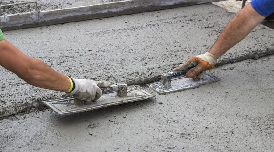 Workers applying concrete with trowels for slab foundation installation, related to plumbing maintenance and structural integrity.
