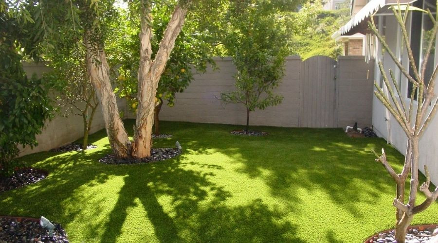 Lush green backyard with manicured artificial grass, surrounded by trees and decorative stones, illustrating a well-maintained outdoor space relevant to plumbing and landscaping discussions.