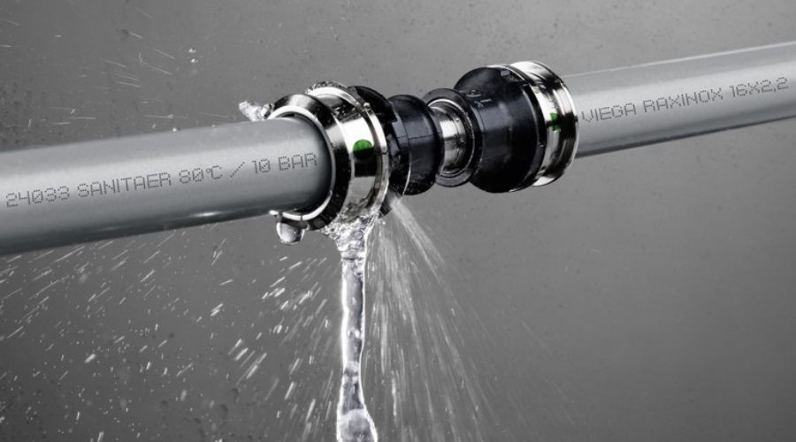 Leaking plumbing pipe with water flowing from a joint, highlighting potential maintenance issues relevant to commercial plumbing services.