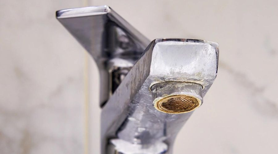 Close-up of a bathroom faucet showing mineral buildup, highlighting hard water issues relevant to plumbing maintenance and treatment solutions.